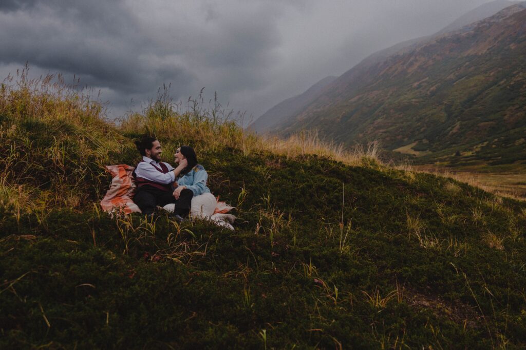 A couple enjoys a moment sitting on the hillside surrounded by mountains in Turnagain Pass, Alaska.