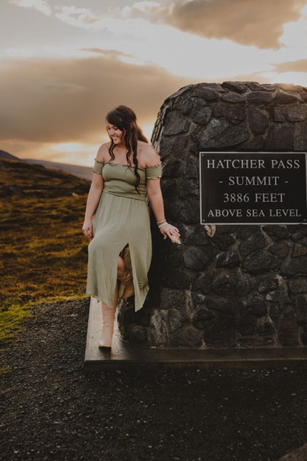 Brooke standing at the summit monument in Hatcher Pass