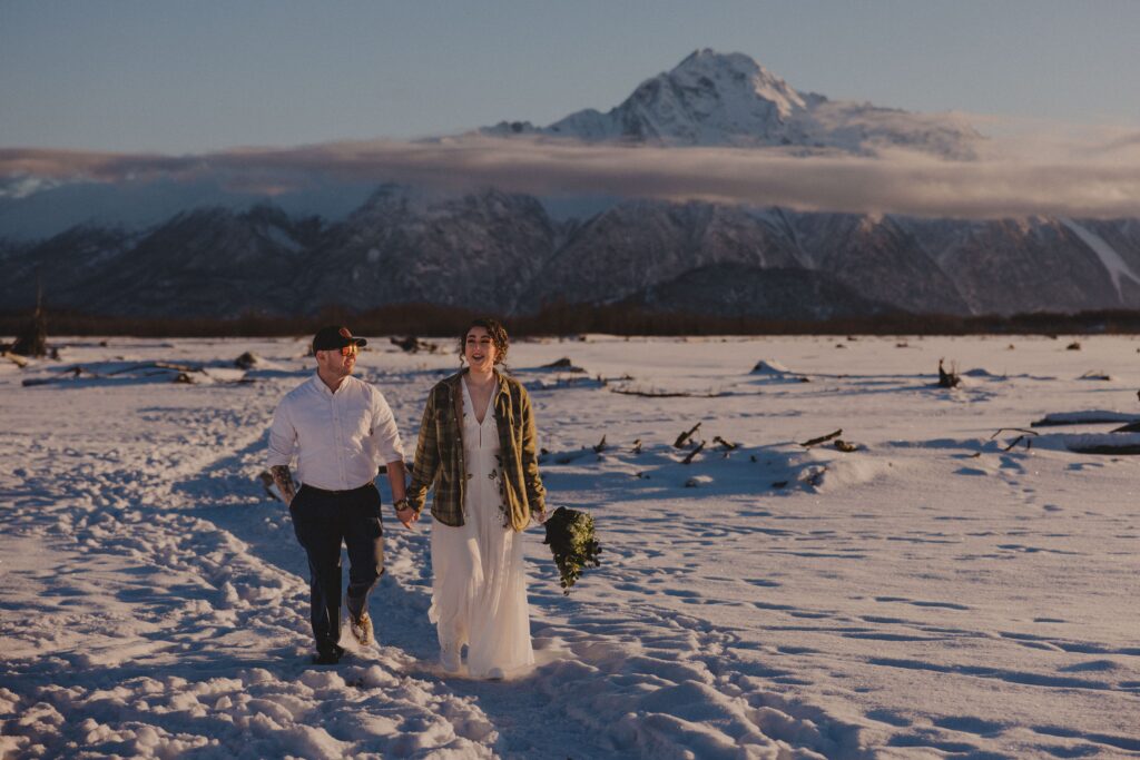 Bride and groom walk in front of Alaskan mountains.