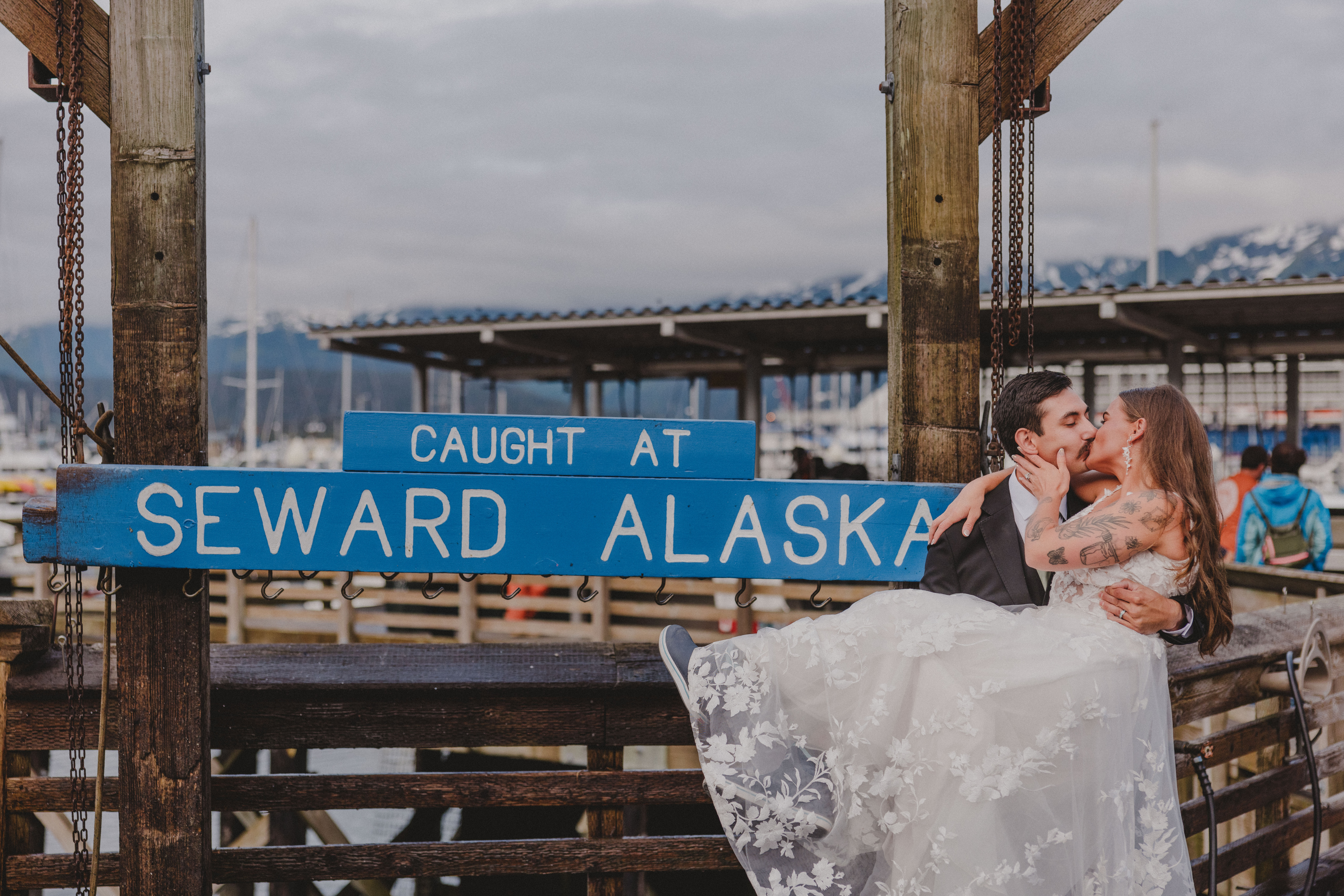 C and B kiss in front of the "Caught in Seward Alaska" sign on the fishing docks after their beach wedding at Lowell Point.